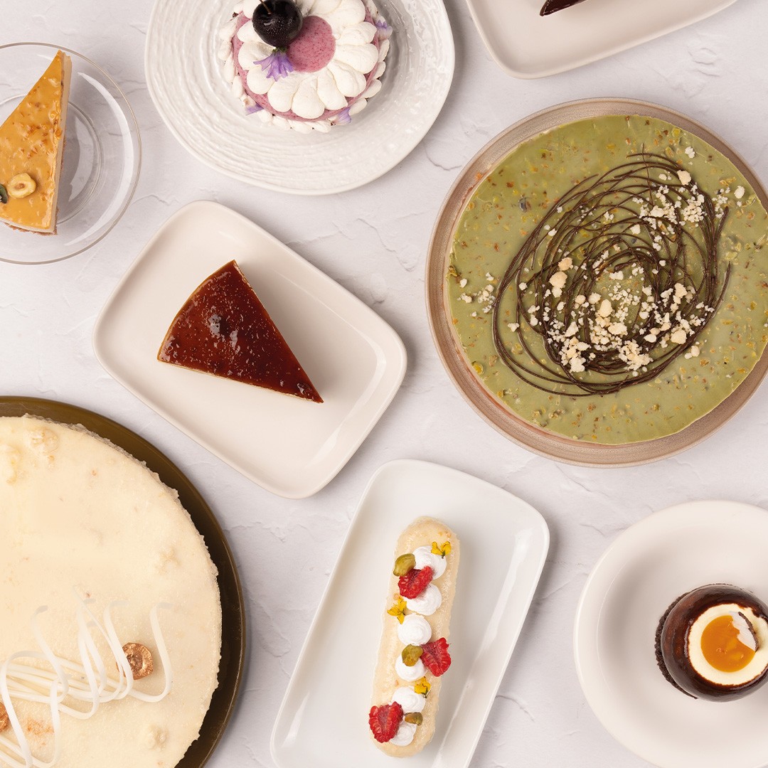 Pogled odozgo na deserte: cheesecake, flan, pistacio torta, eklerи i čašice sa čokoladnim mousseom